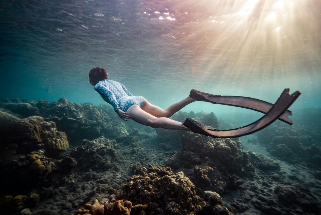 A freediver swims over vibrant coral reefs, soaking in underwater beauty and tranquility.