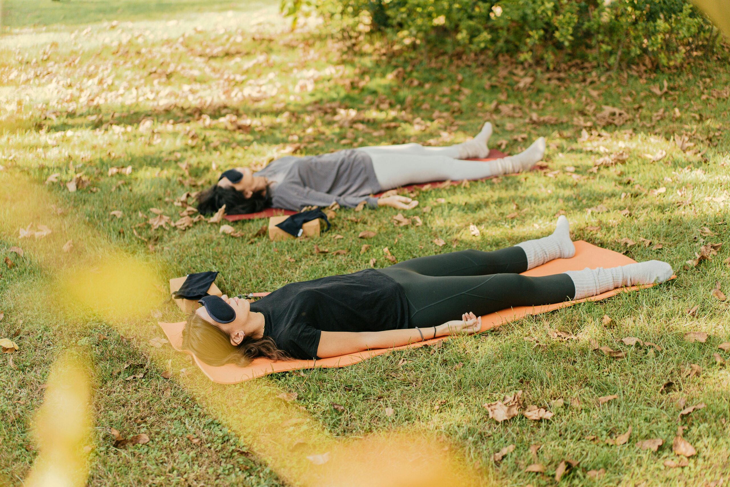 Two women practicing yoga and meditation on grass, focusing on relaxation.